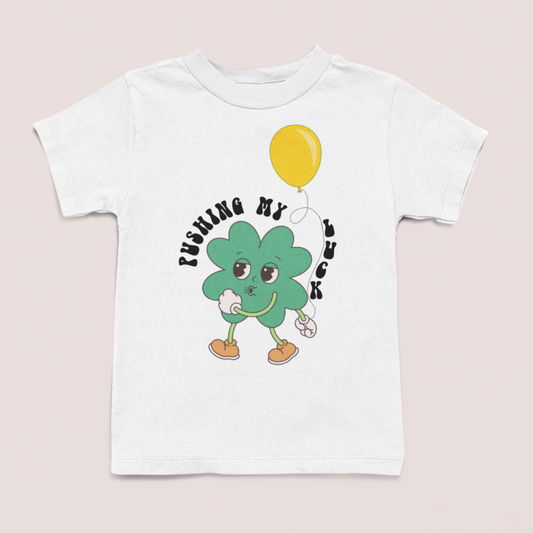 white tshirt with cute clover character holding balance, text: "pushing my luck", part of Lucky charity collection all proceeds donated to National Diaper Bank
